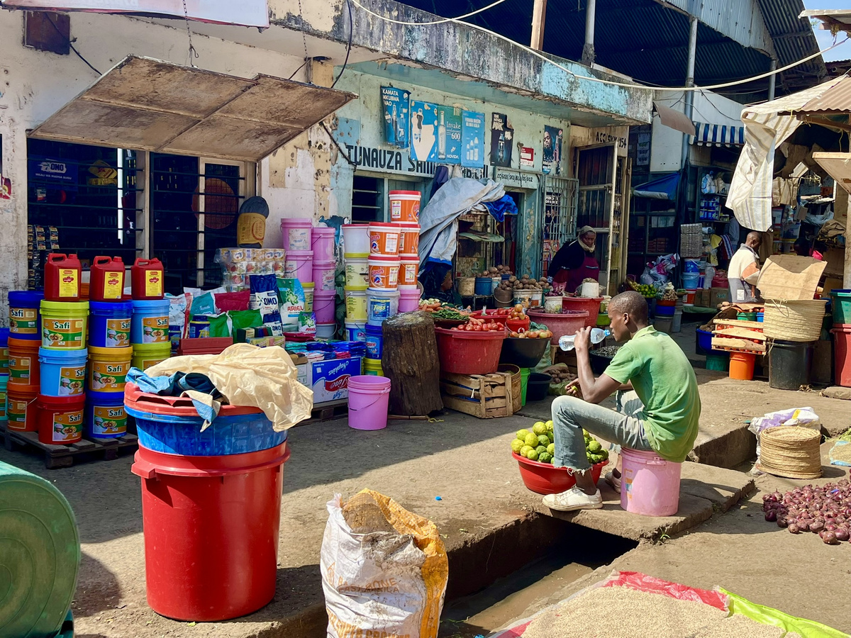 A man sitting on a pink bucket at an African market stall