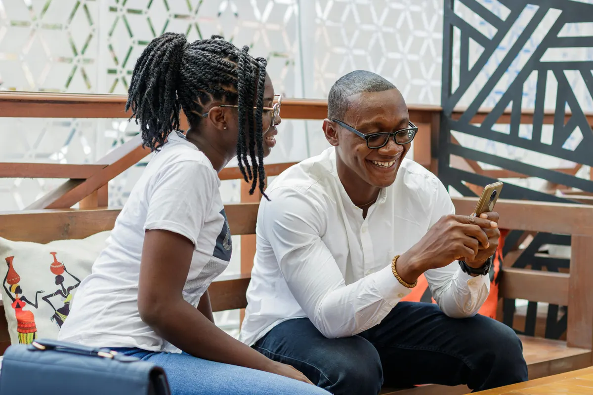 Two smiling African professionals looking at a phone in a bright office