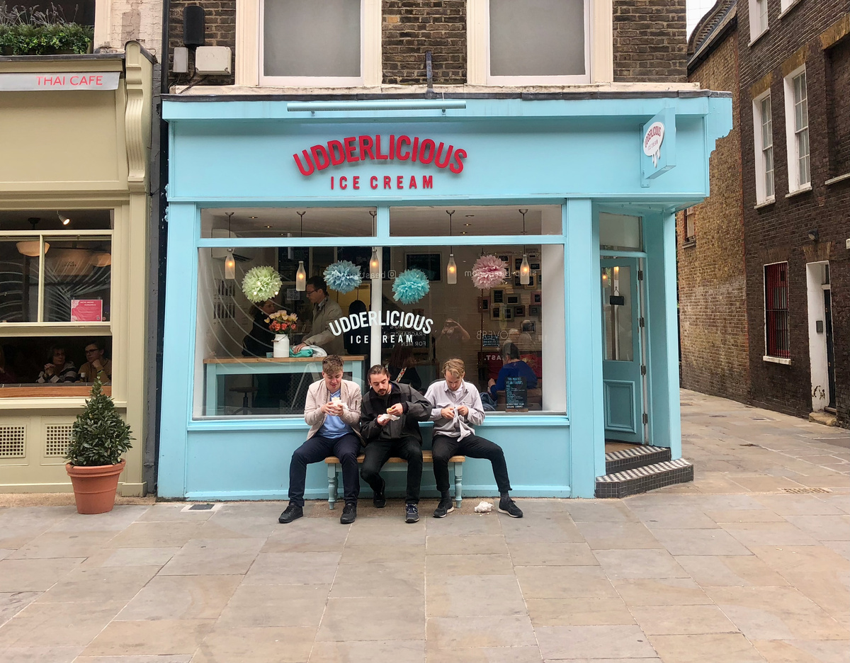 3 Men eating lunch on a bench outside an ice cream shop