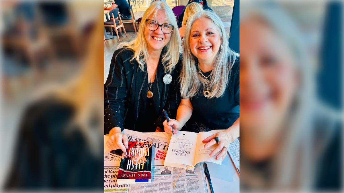 Sue is signing a copy of her book with a friend