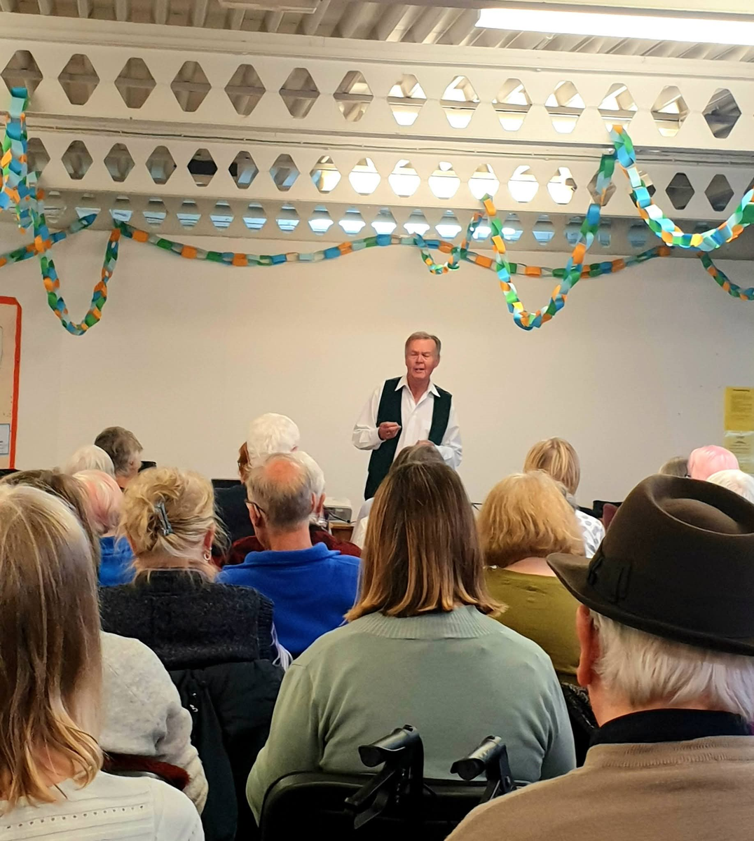 John Eaves speaking to a seated audience in a community hall