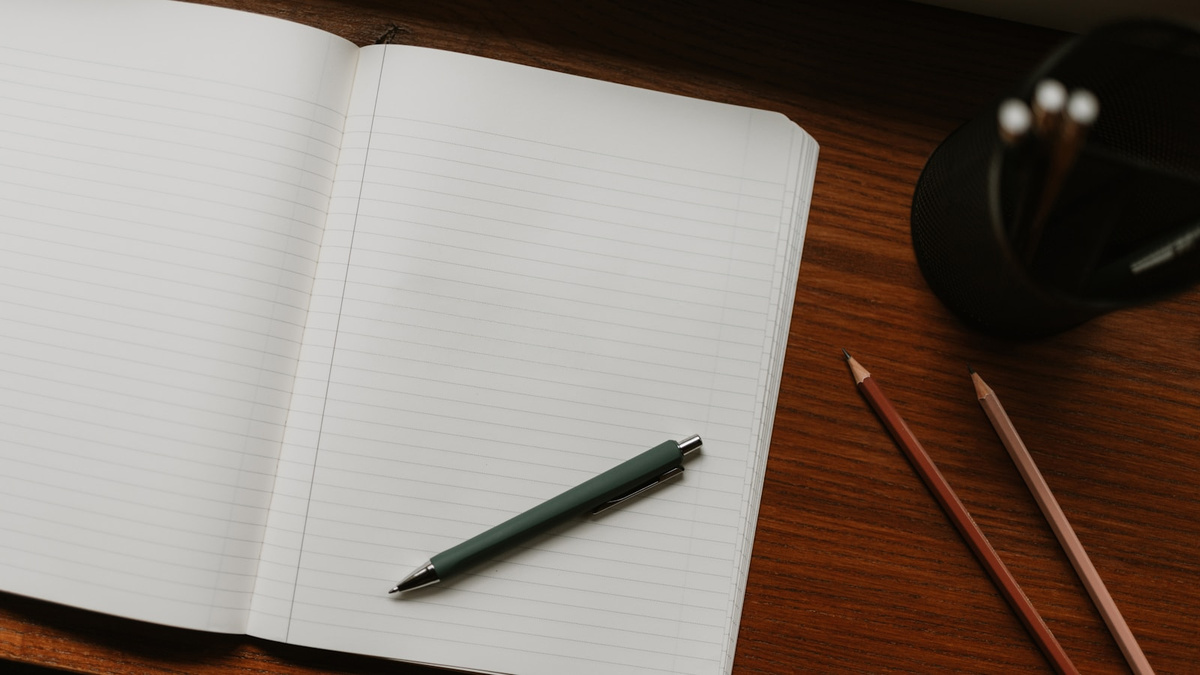An open lined notebook with a pen and pencils on a wooden desk