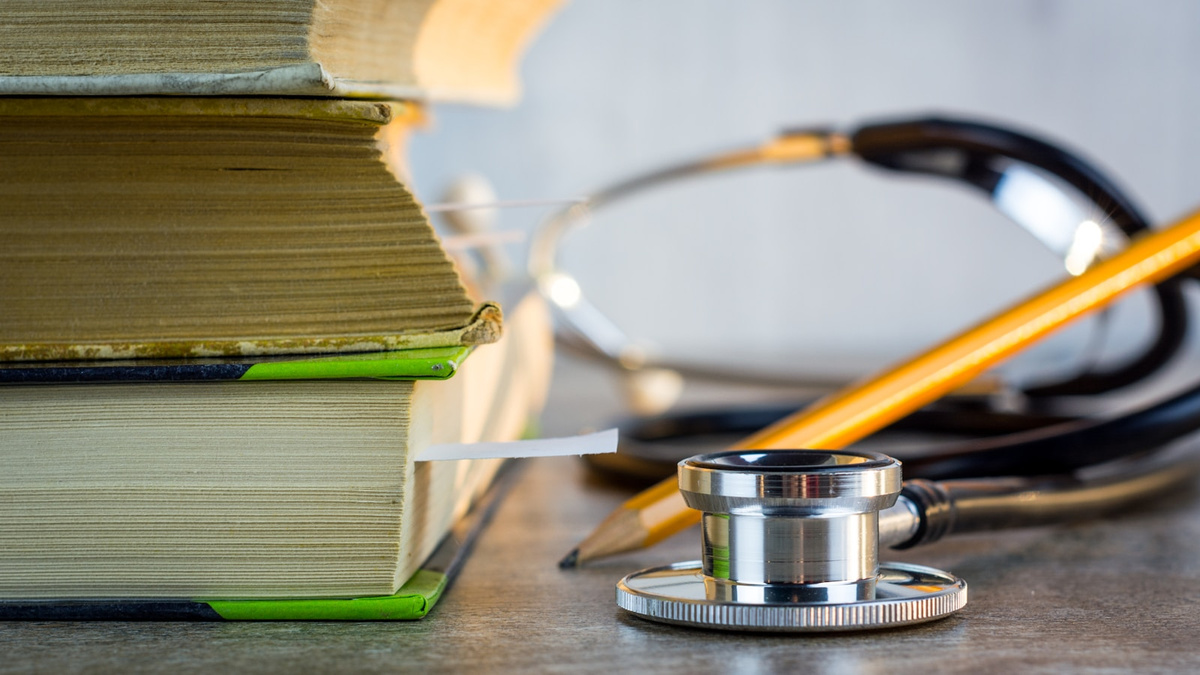 A stethoscope beside a stack of medical textbooks and a pencil