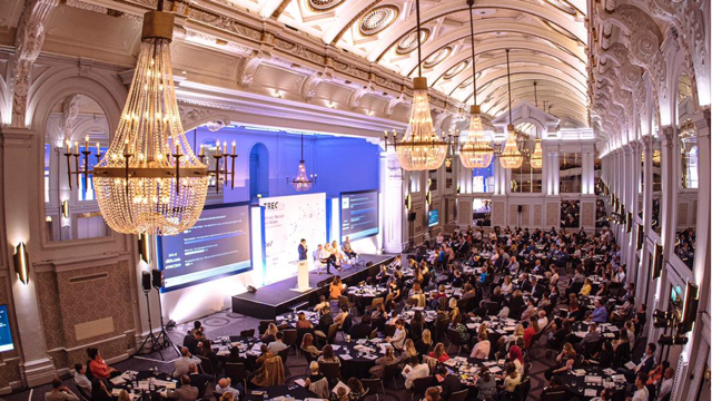 A large conference audience in a chandelier-lit ballroom