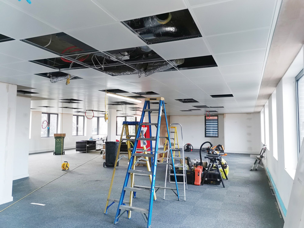 Open-plan office refurbishment in progress with ladders and open ceiling tiles