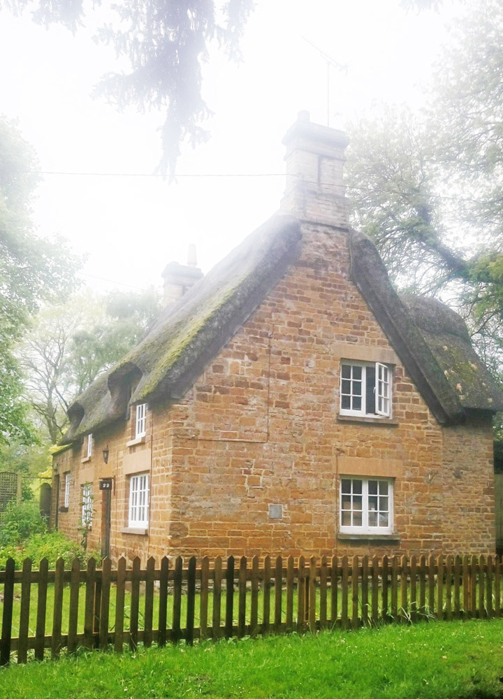Thatched ironstone cottage behind a wooden picket fence