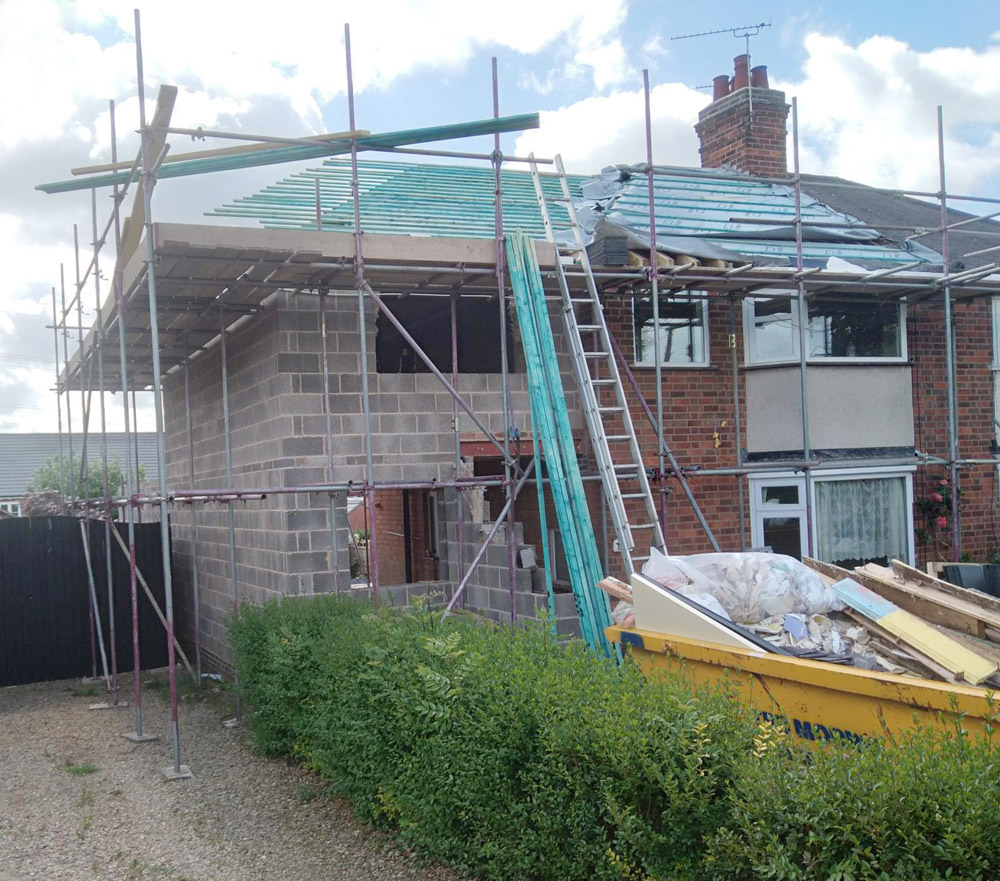 Scaffolding around a house extension under construction with blockwork walls and roof battens