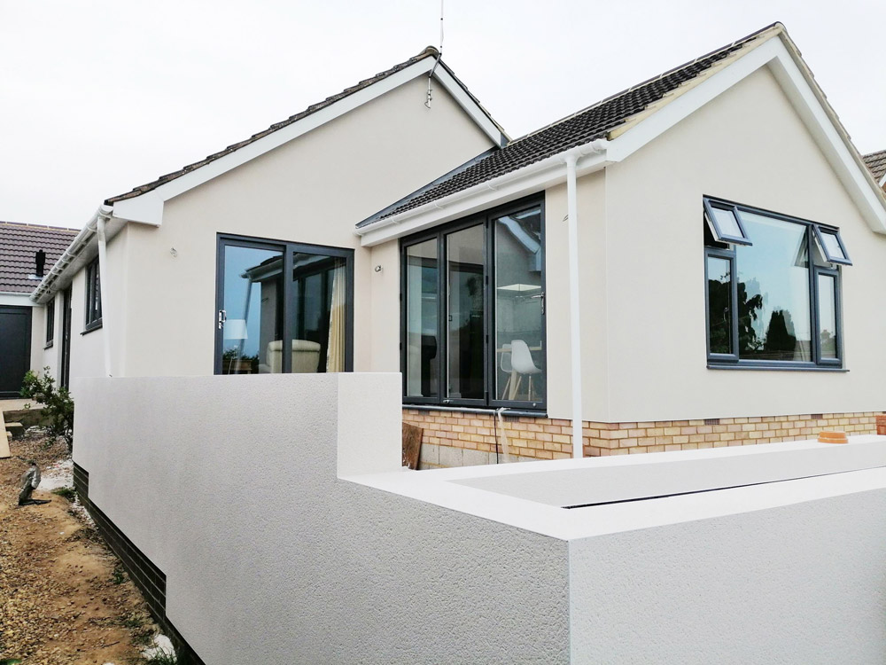 Rendered bungalow extension with large grey-framed windows and a raised terrace