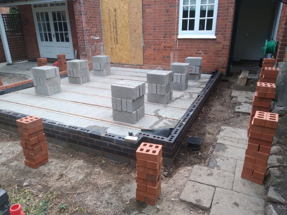 Extension foundations with a beam-and-block floor and brick piers beside a red brick house