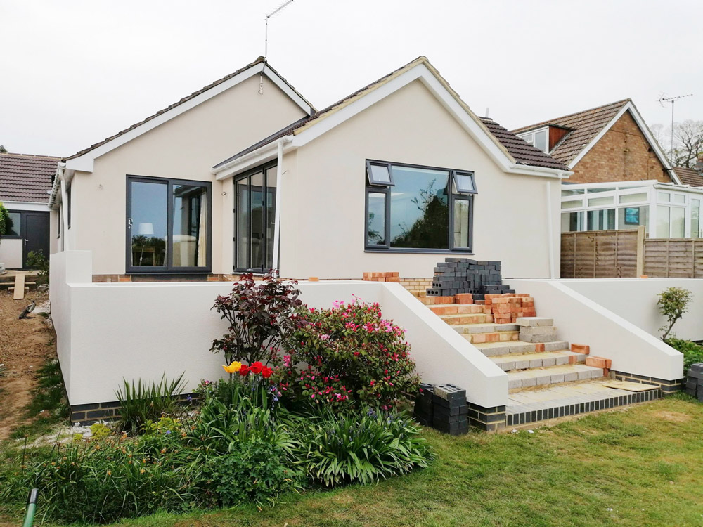 Rendered bungalow with a new extension, brick steps and a planted front garden