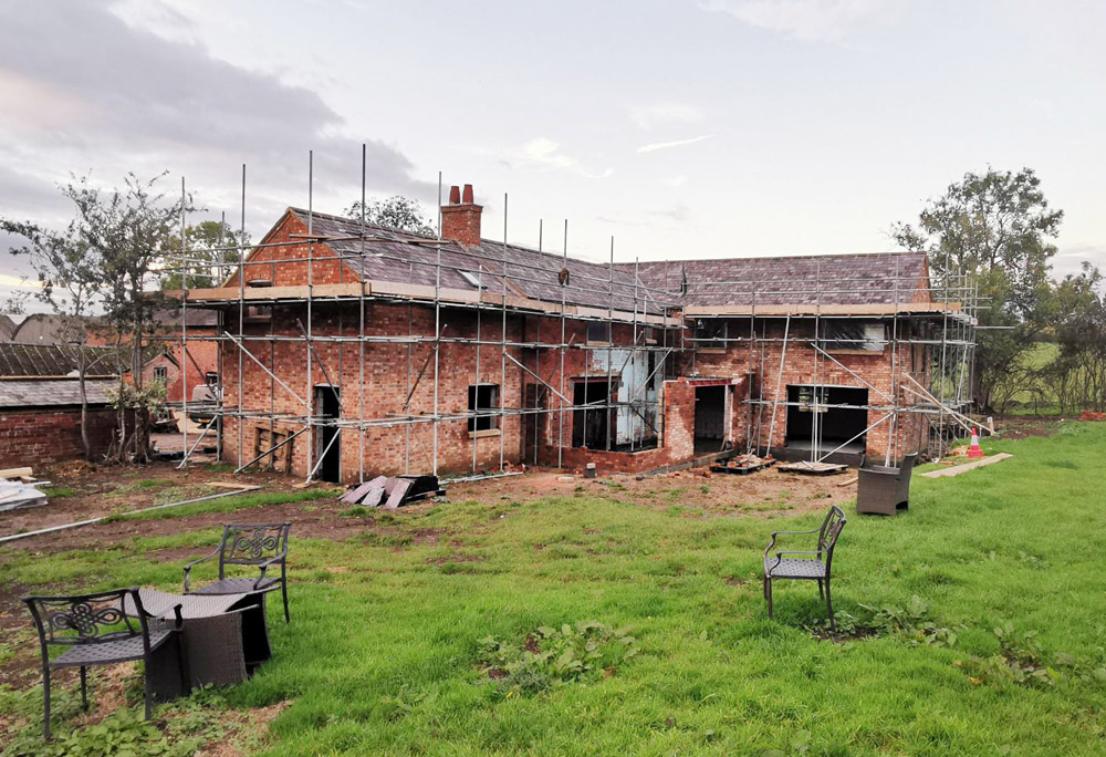 Brick farmhouse under renovation surrounded by scaffolding