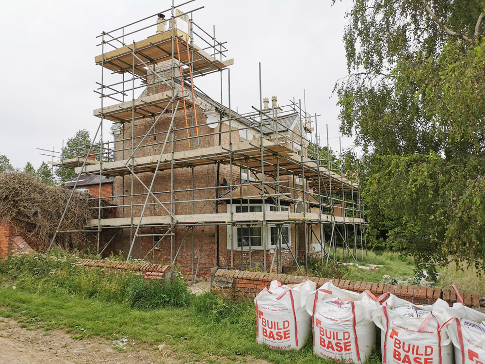 Brick house extension wrapped in scaffolding with bulk bags of materials