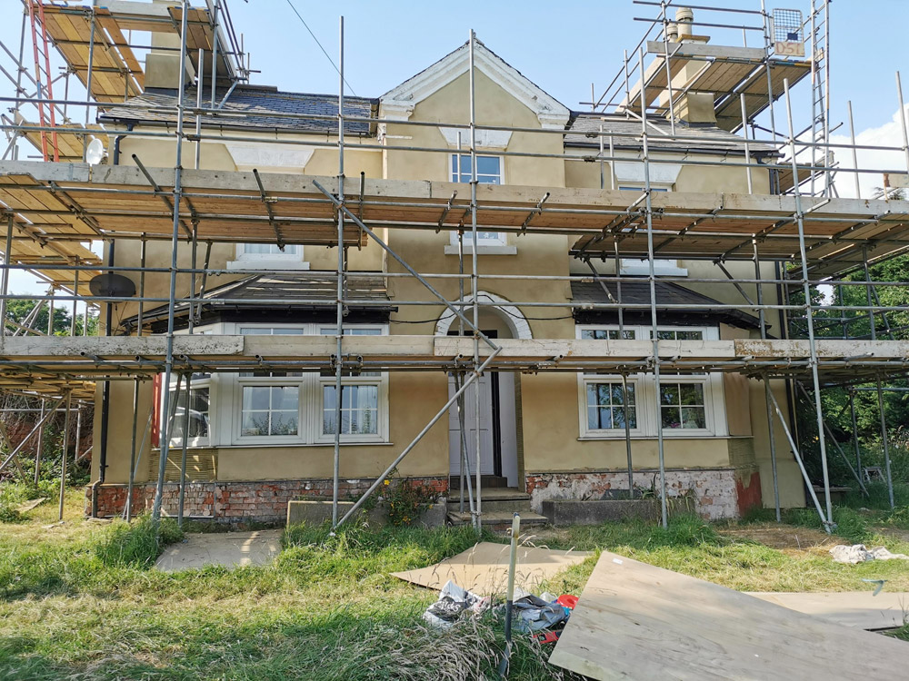 Two-storey rendered house under scaffolding during a renovation