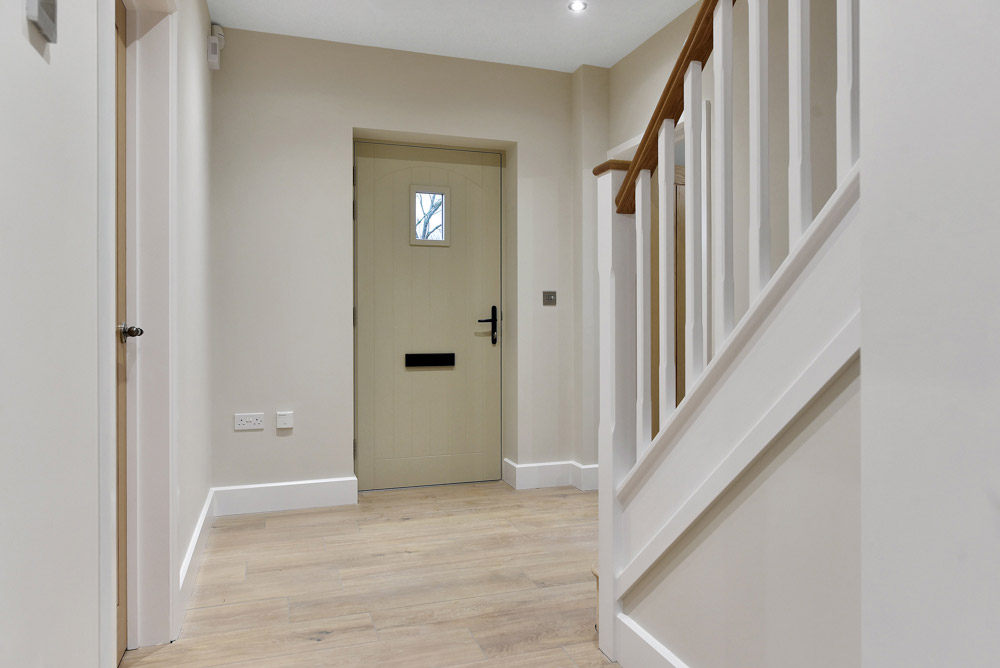 Hallway with oak-effect flooring, a white staircase balustrade and front door