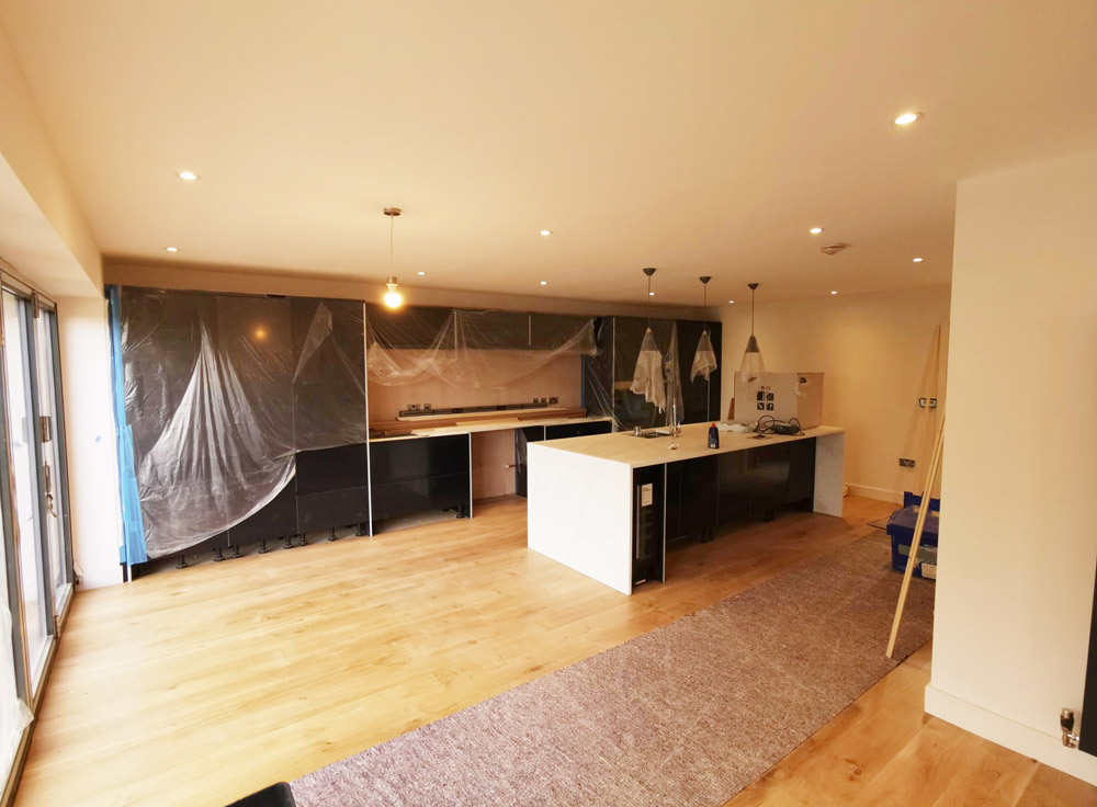 Large kitchen with dark units and oak flooring in a renovated open-plan room