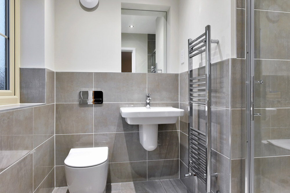 Modern bathroom with grey wall tiles, a wall-hung toilet, basin and chrome towel radiator