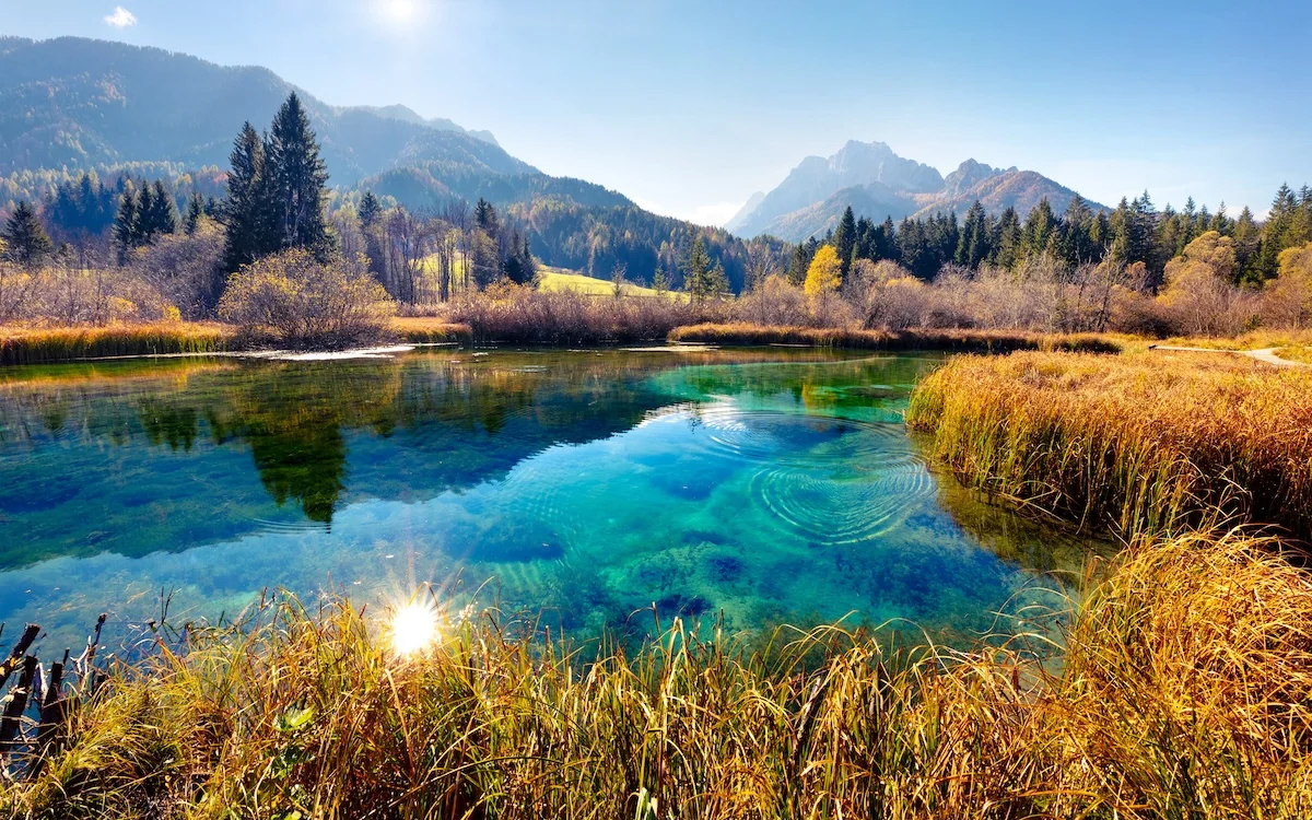 Clear turquoise water reflecting autumn woodland and mountains in Slovenia
