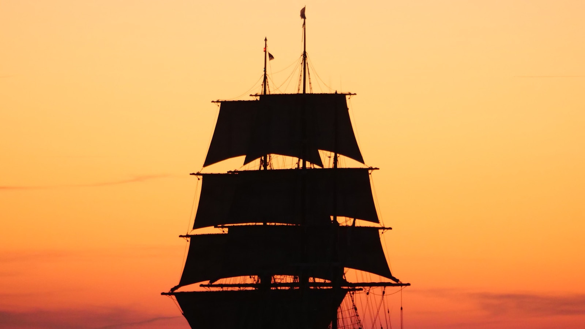 Tall sailing ship silhouetted against an orange sunset