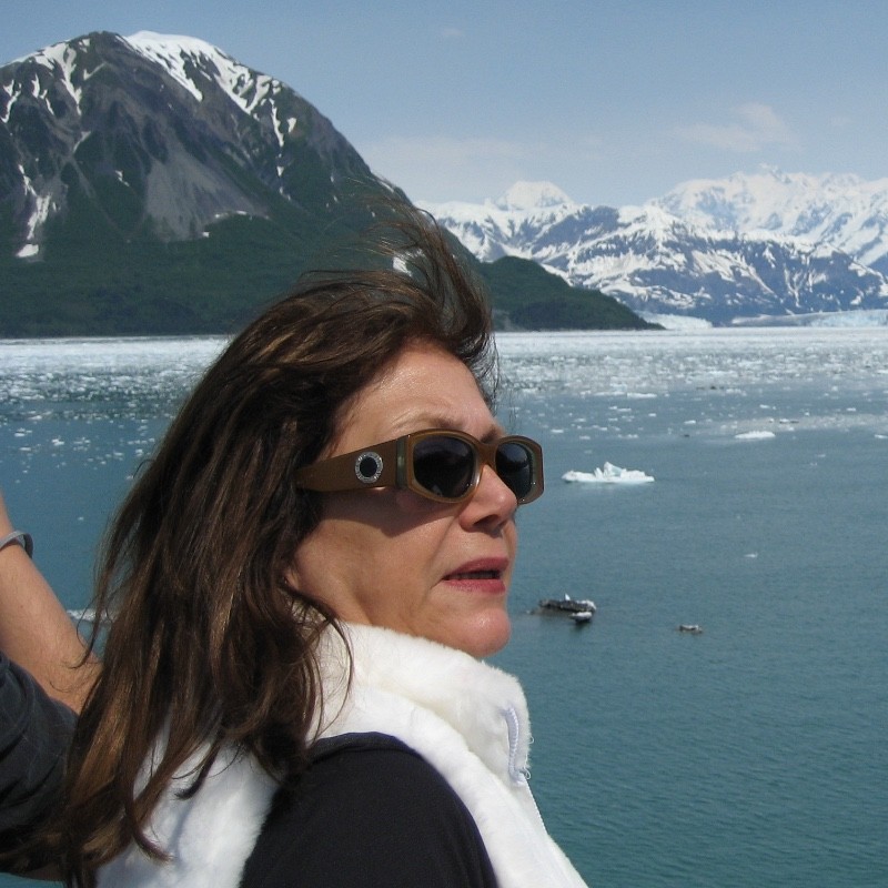 Stella Darvey Joory wearing sunglasses on a boat, with snow-capped mountains and icy water behind her