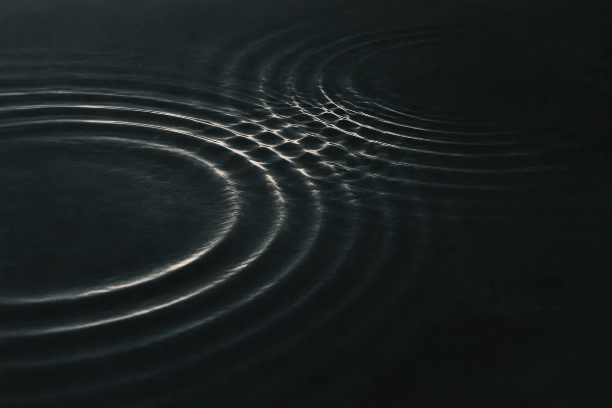 Intersecting pale ripples forming an interference pattern on dark water.