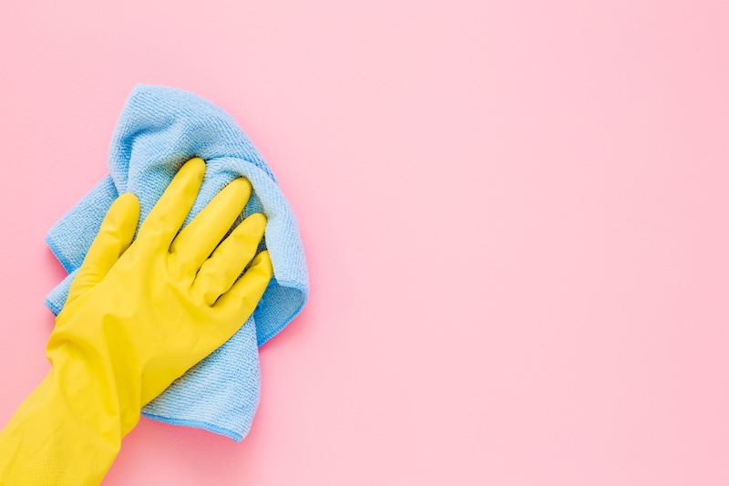 Yellow marigold glove wiping a blue cloth on a pink surface