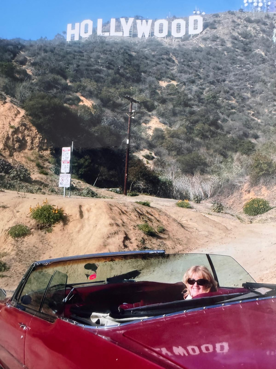 Carole Ryder in a red convertible beneath the Hollywood sign