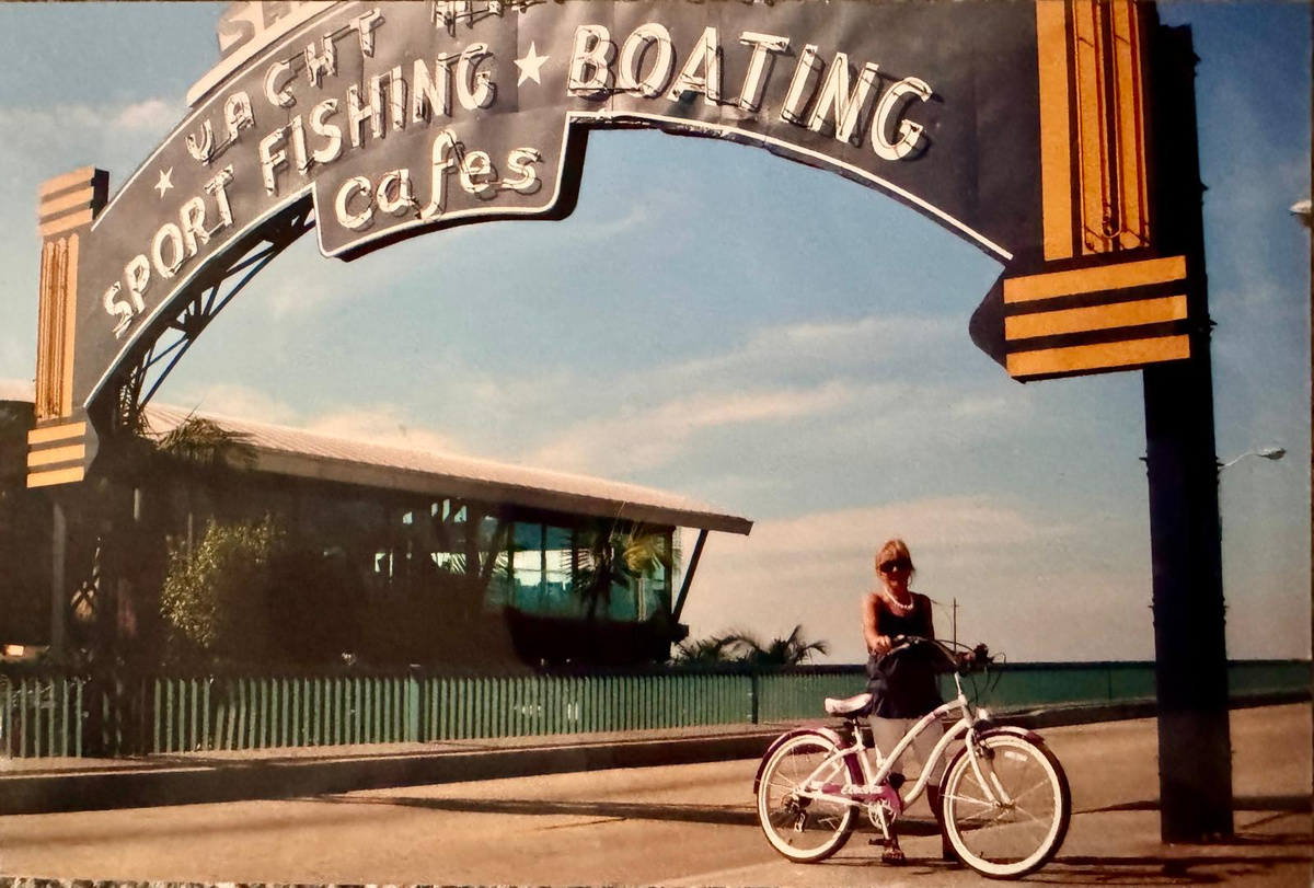 Carole Ryder with a bicycle beneath a vintage waterfront sign