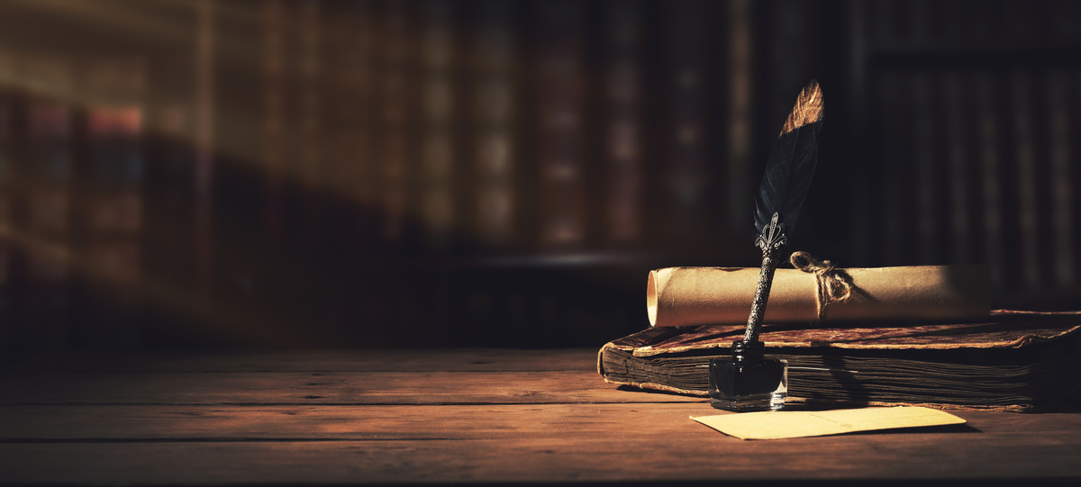 A quill and ink bottle beside an old book and rolled parchment