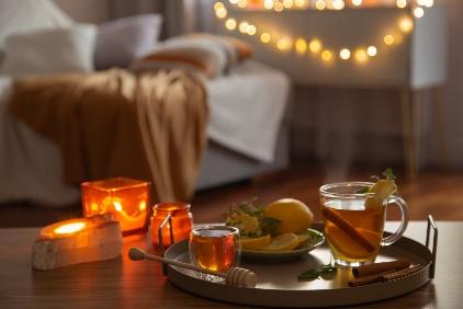 Cups of herbal tea with lemon and cinnamon on a tray beside glowing candles and fairy lights