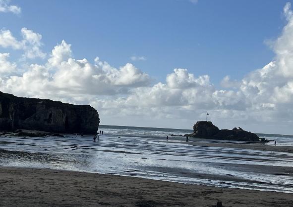 Perranporth beach in Cornwall: dark rocks, blue sea and wet golden sand under a cloudy sky