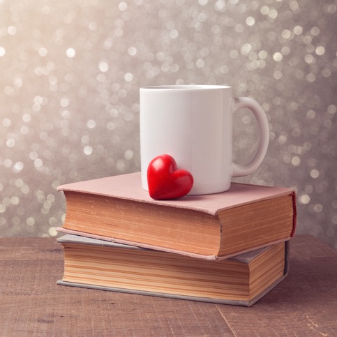 White mug with a red heart, resting on a stack of books