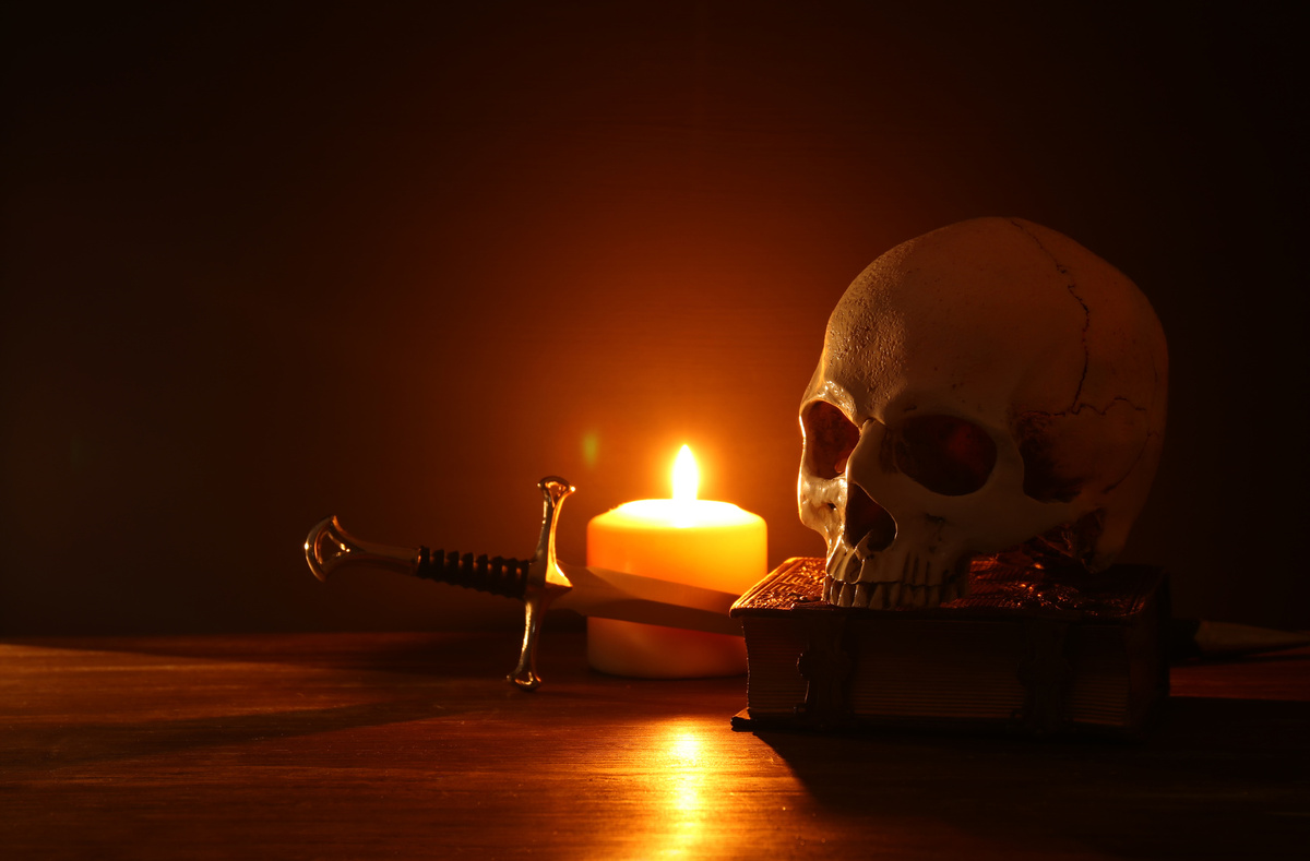 A candlelit skull on a book beside a theatrical dagger